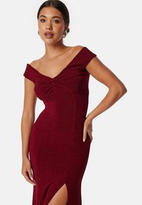 Burgundy avaxeln klänning med en tvistknut bodice, figurnära silhuett, framsidan lårslits och subtil glittrig textur.