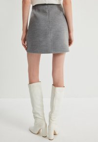 Grå texturerad minkjol med en åtsittande midja, tillsammans med höga vita läderklackar med blockhälar, som visar upp ett mjukt material och en strukturerad design.