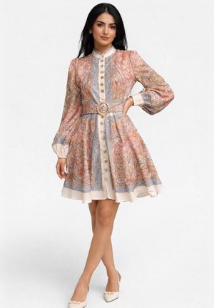 Kobieta w sukience z paskiem, z długim rękawem, do kolan, z wielobarwnym wzorem paisley i ozdobnymi guzikami z przodu.