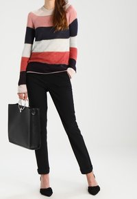 Multicolore gestreepte trui in roze, marineblauw en crème, gecombineerd met zwarte broeken en een zwarte totebag. Zachte textuur, ronde halslijn.