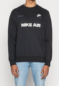 Svart sweatshirt med rund hals, prydd med "NIKE AIR" i vit text och logotypdetaljer. Mjukt tyg med ribbade ärmslut och nederkant.