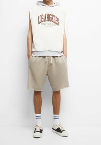 Sleeveless beige hoodie with "LOS ANGELES NEW SEASON" print, paired with light beige shorts, white and blue striped socks, black and white sneakers.