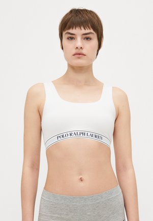 Balta sporta krūšturis ar platiem siksniņām un zemu izgriezumu. Izceļas ar tumši iezīmētu "Polo Ralph Lauren" logo uz elastīgās joslas.