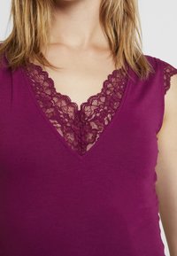 Top de tirantes burdeos con diseño de escote en V que presenta un delicado encaje en el cuello. La tela se ve suave y ajustada.