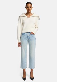 Maglione bianco a coste con cappuccio oversize, chiusura con zip, abbinato a jeans blu chiaro a gamba dritta e tacchi a punta neri.