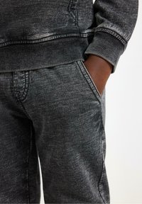 Jogger in denim nero con finitura testurizzata, dotati di una cintura comoda e tasche laterali, con un aspetto sbiadito e vissuto.