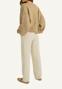 Beige Chunky-Strickpullover mit einer verkürzten Passform, oversized Ärmeln, kombiniert mit hellbeigen, weiten Hosen und flachen Schuhen. Schlichtes Design.