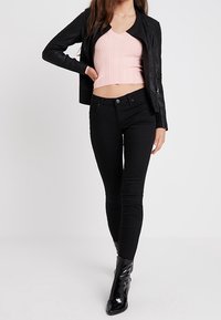 Černá kožená bunda, růžový žebrovaný krátký top, černé úzké džíny a černé špičaté kotníkové boty. Oblečení má hladký a přiléhavý střih.
