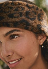 Brunt leopardmönstrat diadem gjort av mjup päls, med en slät textur och ett kontrasterande svart mönster. Guldfärgat ringörhänge med en pärldetalj.