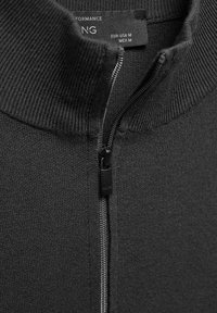 Suéter negro con cremallera y cuello alto, con textura acanalada y tela lisa con herrajes de cremallera metálica. Etiqueta de cuidado visible.