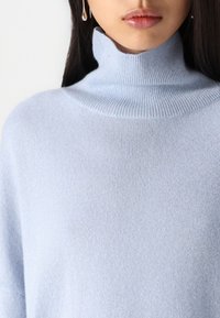 Jasnoniebieski, prążkowany sweter z wysokim kołnierzem i miękką teksturą, z luźnymi rękawami i minimalistycznym designem.
