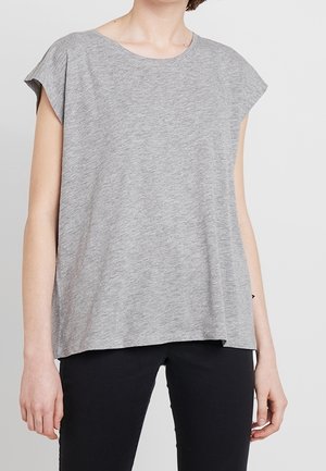 Woman wearing a loose-fitting short-sleeve gray top with a round neckline and black pants against a plain background.