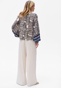 Lichte crèmekleurige linnen broek met wijde pijpen, gecombineerd met een blouse met een patroon van zwarte golvende lijnen en blauwe accenten op de mouwen.