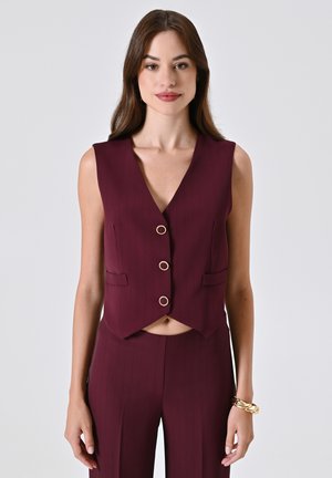 Gilet senza maniche bordeaux con scollo a V, caratterizzato da tre bottoni circolari dorati e due tasche frontali, abbinato a pantaloni coordinati.