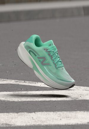Светлозелен маратонка New Balance във въздуха над асфалт с бели пътни маркировки, показваща движение и детайли за сцепление.