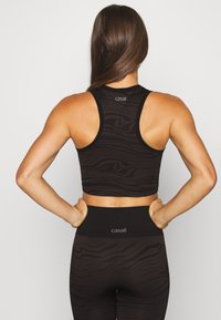 Top deportivo negro corto con un patrón de cebra texturizado y un logo en la parte posterior, combinado con leggings de cintura alta a juego.