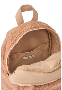 Rucsac deschis de textura teddy bej, cu un buzunar interior din material și mâner în vitro, arătând eticheta brandului Liewood în interior.