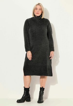 Vestido negro de punto con cuello alto, mangas largas y aberturas laterales, que presenta una tela texturizada. Se lleva con botas negras hasta el tobillo.