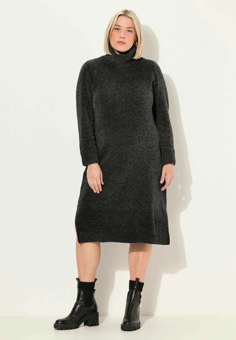 Robe en tricot noir à col roulé avec manches longues et fentes sur les côtés, fabriquée dans un tissu texturé. Portée avec des bottines noires.
