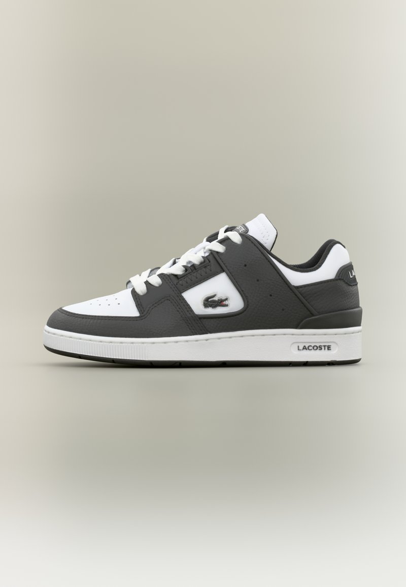 Sapatilha Lacoste em preto e branco com atacadores brancos, biqueira perfurada, logótipo de crocodilo na lateral e sola com marca em fundo neutro.