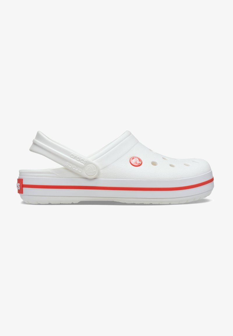 Sabot Crocs blanc avec des trous de ventilation, une bande rouge sur la semelle, une bride de talon réglable et un logo circulaire rouge sur le côté.