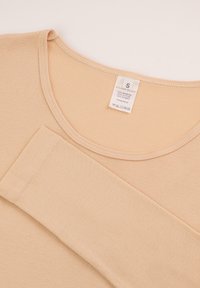 Beżowa koszula z długim rękawem i okrągłym dekoltem, wykonana z miękkiej bawełny, z metką wskazującą rozmiar S oraz instrukcjami prania.