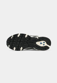 Semelle de chaussure noire et blanche avec motif de grip texturé et accents bleus au talon, présentée sur un fond clair uni.