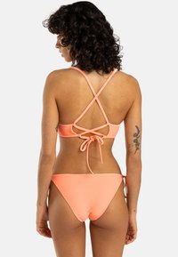 Koralový bikiny se žebrovaným vzorem, křížovým zadním dílem a zavazováním. Nastavitelné ramínka a design spodního dílu s minimálním pokrytím. Hladká textura po celém výrobku.