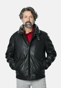 Chaqueta de cuero negra con un suave cuello de piel gris, dos bolsillos frontales y cierre de cremallera. Se lleva sobre una camisa roja de corte relajado.