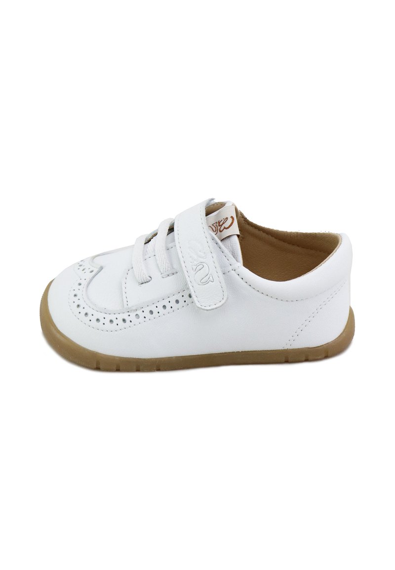 Zapato de cuero blanco con cordones y una tira de velcro, que presenta detalles perforados y una suela de goma marrón. Diseño de punta redondeada.