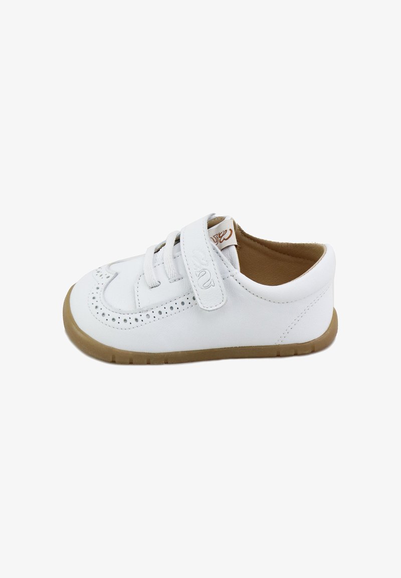 Zapato de cuero blanco con cordones y una tira de velcro, que presenta detalles perforados y una suela de goma marrón. Diseño de punta redondeada.