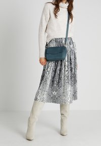 Ljusgrå, ribbad stickad tröja, knälång, svartvit ormskinnsmönstrad veckad kjol, blå axelremsväska och krämfärgade knähöga stövlar.