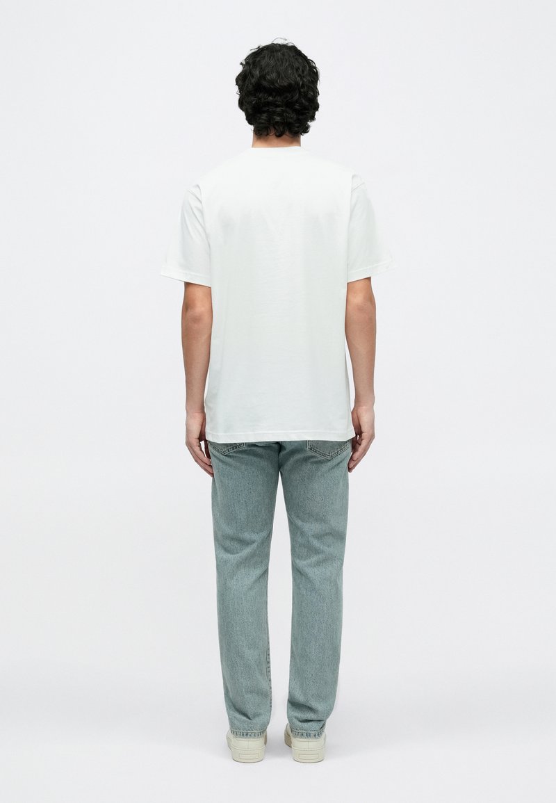 Hvid bomulds-t-shirt med korte ærmer, set bagfra, kombineret med lyseblå denimjeans og sneakers i neutrale farver.