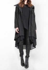 Schwarzer, schichtweise gestalteter Mantel mit Kapuze und Druckknöpfen, getragen über einem schwarzen langen Oberteil und eng anliegenden schwarzen Lederhosen. Besitzt einen flatternden Saum.
