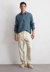 Lightweight blue linen shirt with a chest pocket, paired with cream-colored linen trousers and beige shoes. Simple design and relaxed fit.