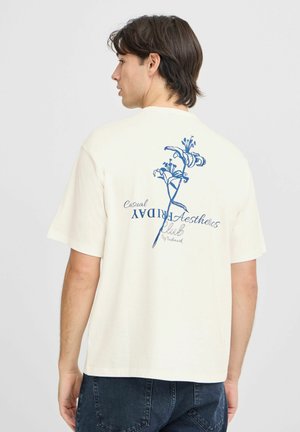Kremfarget bomull t-skjorte med blått blomsterdesign og tekst på ryggen. Korte ermer og avslappet passform.