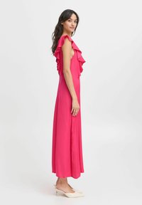 Rosa maxiklänning med volangärmar och en slank silhuett, gjord av lättviktig tyg. Matchad med krämfärgade spetsiga klackar.