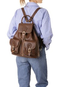 Bruine leren rugzak met een klep, twee voorzakken en gesp-sluitingen. Het heeft een gestructureerde afwerking en verstelbare banden.