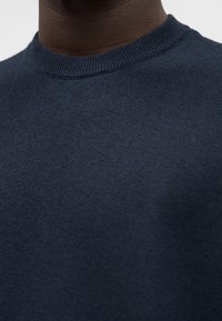 Μπλε σκούρο πλεκτό πουλόβερ με ριμπ πλεκτό λαιμόκοψη, που αναδεικνύει μια λεία υφή και ομοιόμορφη ραφή σε όλο το ύφασμα.