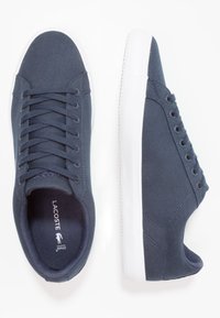 Paire de baskets en toile bleu foncé avec semelles blanches, l'une vue du dessus et l'autre de côté, sur fond blanc.