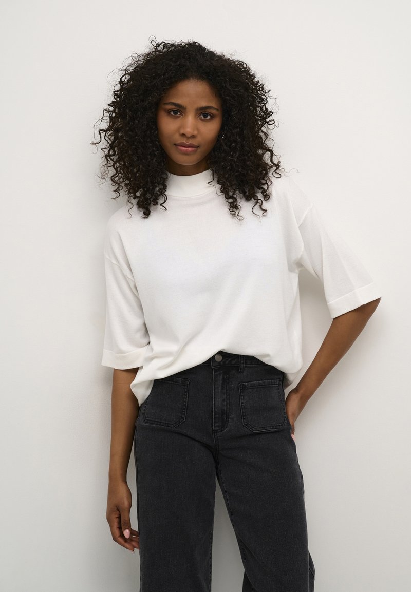 White high-neck oversized t-shirt made of soft fabric, paired with black high-waisted jeans featuring pockets and a classic button closure.