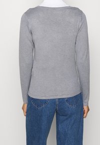 Top gris de manga larga hecho de un suave tejido de punto, presenta un escote redondeado y una silueta ajustada, combinado con unos pantalones vaqueros azul de cintura alta.