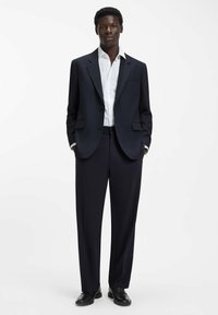 Granatowy garnitur dwuczęściowy z dopasowaną marynarką, białą koszulą oraz pasującymi spodniami. Gładka tkanina, klasyczny krój i minimalne zdobienia.