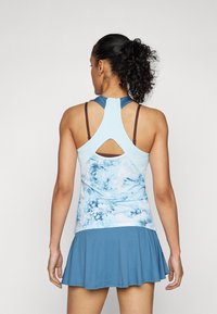 Lyseblå treningssinglet med racerback-design, har en utskåret bakside og et mønstrete nedre kant. Brukt sammen med et matchende blått skjørt.