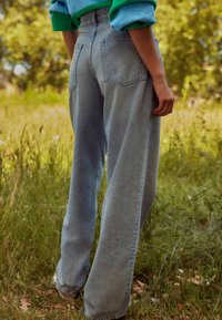 Jeans cu talie înaltă, cu picioare largi, din denim albastru deschis decolorat, având două buzunare la spate și ușoare deteriorări pe cusături.