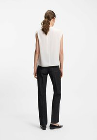 Weißes ärmelloses Blusenshirt kombiniert mit dunklen, schmalen Jeans und flachen schwarzen Schuhen, von hinten betrachtet, zeigt ein sauberes Design mit minimalen Details.