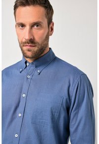 Camisa azul abotonada hecha de tela texturizada, con un bolsillo en el pecho, pequeños botones y un diseño de cuello clásico.