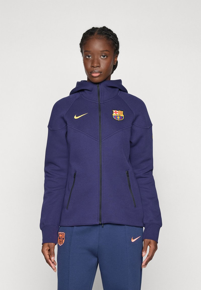 Lila Zip-Hoodie mit Kapuze, versehen mit dem Barcelona-Wappen und dem Nike-Logo in Gold. Strukturierter Stoff und zwei mit Reißverschluss versehenen Seitentaschen.