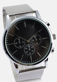 Silver stainless steel watch with a black dial, three sub-dials, and a mesh strap. Features minimalist hour markers and a crown on the side.