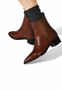 Botines de cuero marrón con puntera afilada y un tacón bajo en bloque, con acentos verticales con ribetes en los laterales.